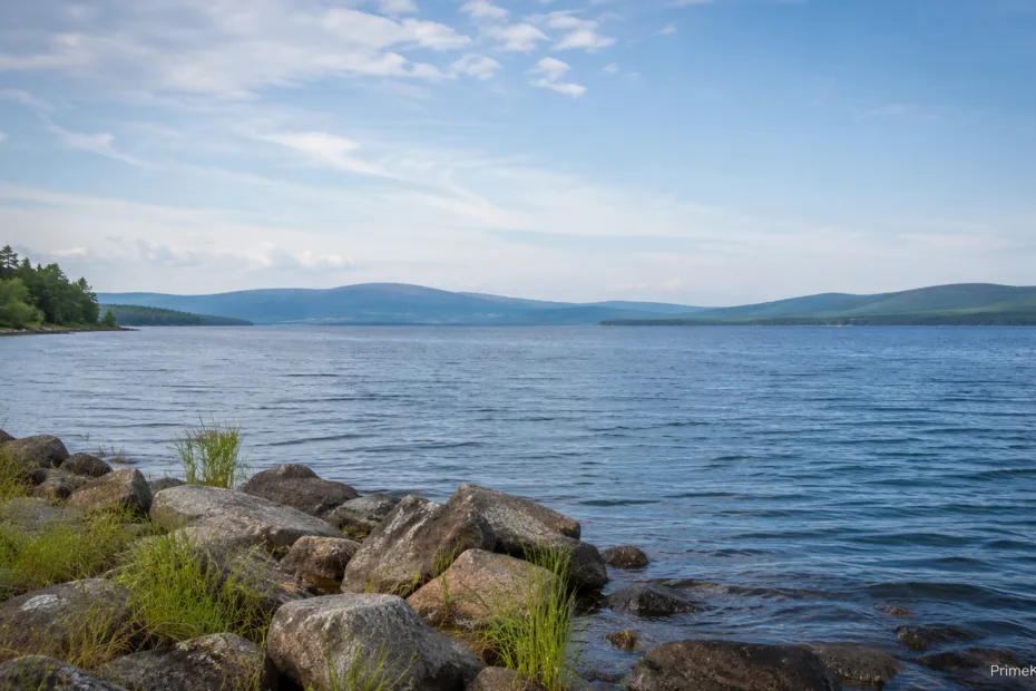 Crystal-clear lake water laps against rocks along the shoreline with distant mountains in the background.
